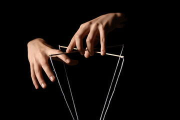 Female puppeteer with strings on black background, closeup