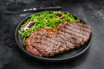 Roasted dry aged New York strip steak served with fresh arugula on textured dark stone, highlighting rich flavor and perfect grill marks.