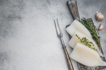 Raw calamari arranged with herbs on weathered wood against a gray stone backdrop ideal for culinary seafood stock concepts.
