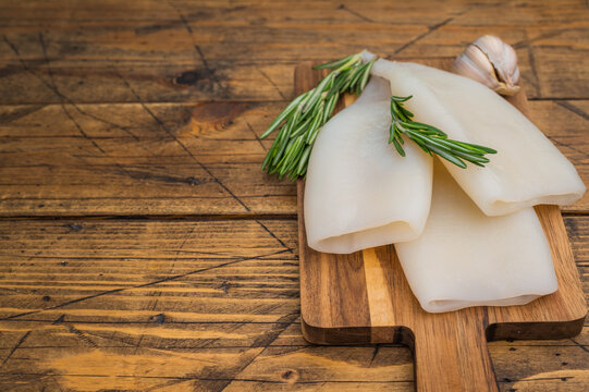 Raw calamari and fresh rosemary on vintage wood board captured for culinary design seafood menus and Mediterranean style visuals