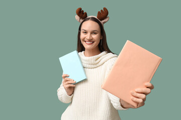 Obraz premium Happy young woman in Christmas reindeer horns with books on turquoise background