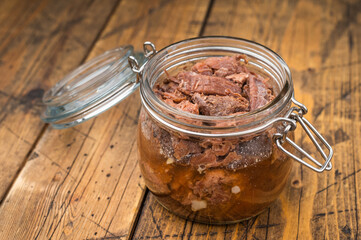 Rustic venison preserved stew in a glass jar with garlic, thyme and pepper on a wooden board. Hearty wildgame meat with rich slowcooked flavor.