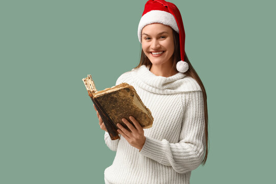 Happy young woman in Santa hat with old book on turquoise background. Christmas concept