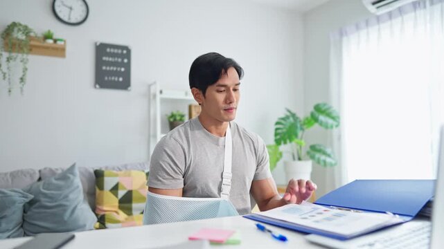 Injured Asian businessman wearing hand splint while working from home.