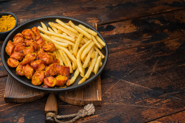 Sliced currywurst, wurst in curry sauce with crispy pommes on dark wood surface ideal for restaurant menus comfort food ads and culinary content.