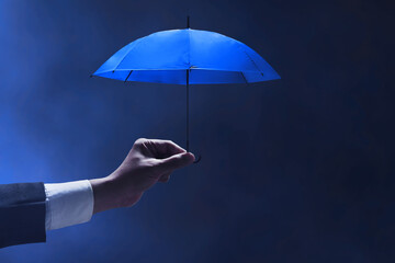 Businessman hand holding blue umbrella on dark background