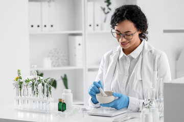 Pretty young African-American female biologist with mortar, pestle and plants working in lab
