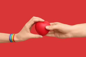 Female hands with rainbow ribbon and heart on red background. LGBT concept
