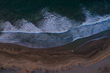 Aerial View of Foaming Waves Crashing on Sandy Beach