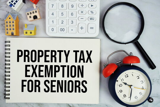 Property Tax Exemption For Seniors text written on notepad with house model, magnifying glass and alarm clock on marble background