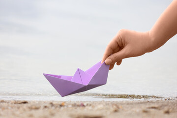 Young woman putting lilac paper boat on water outdoors, closeup