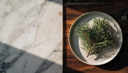 Elegant holiday table setting showcasing fresh pine branch on minimalist plate with marble and wood textures, capturing a cozy, modern Christmas aesthetic