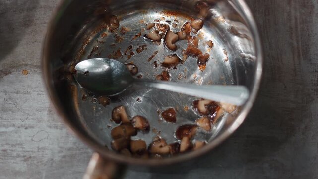 Fresh shiitake mushrooms simmering in a stainless steel pot with a spoon seen from above