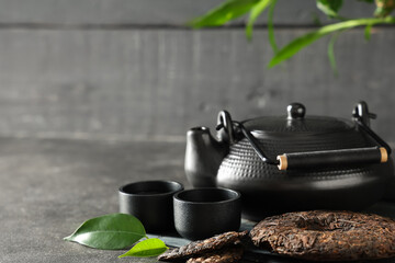 Bamboo mat with dry pressed puer tea, cups and teapot on grey grunge table against wooden wall