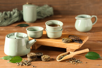 Tray with dry pressed puer tea, teapot, cups and scoop on wooden background