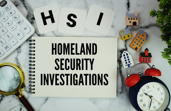 HSI Homeland Security Investigations text written on notepad with house model, calculator, magnifying glass and alarm clock on marble background