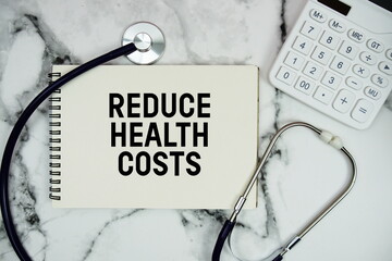 Reduce Health Costs text written on notepad with stethoscope and  calculator on marble background