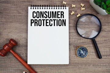 Consumer Protection message written on notepad with wood gavel and magnifying glass flat lay on wooden background
