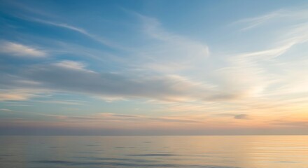 Naklejka premium Calm ocean waters reflecting soft pastel colors of serene morning or evening sky horizon.