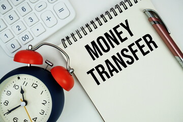 Money Transfer text written on notepad with alarm clock, magnifying glass and calculator on marble background
