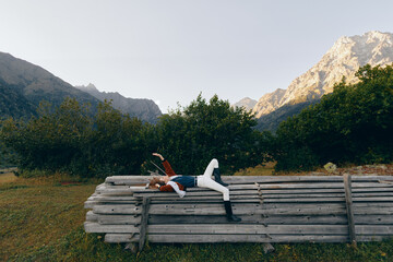 Fototapeta premium Person woman lying on stacked logs in a meadow, enjoying nature and mountains view, relax outdoors among trees and wooden pile for peaceful countryside rest and leisure.