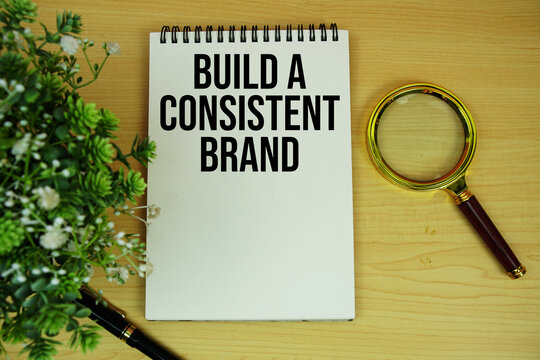 Build a Consistent Brand Message text written on notepad with magnifying glass flat lay on wooden background