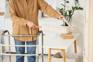 Mature woman with walker and pp-duster cleaning table in bedroom