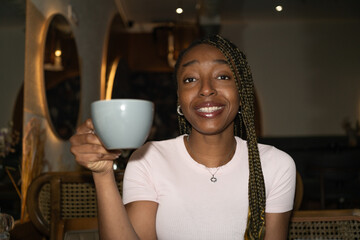 Happy black woman in a restaurant drinking coffee and smiling