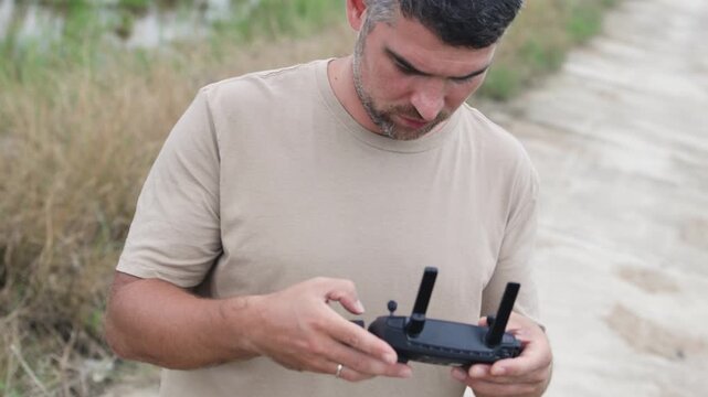 A dark haired man holds a drone remote control in his hands.