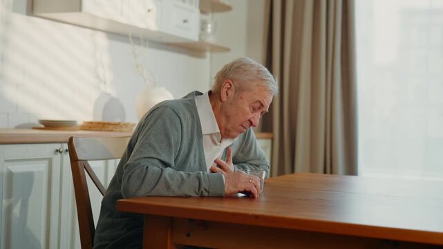 Old man feeling heartache and high blood pressure portrait of senior in kitchen. Health in old age, diseases associated with aging, heart attack and high blood pressure, virus causing pneumonia