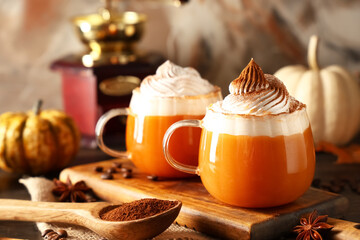 Glass cups of orange pumpkin latte with whipped cream and coffee beans on wooden table