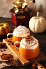 Glass cups of orange pumpkin latte with whipped cream and coffee beans on wooden table