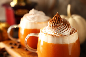 Glass cups of orange pumpkin latte with whipped cream on beige background, closeup