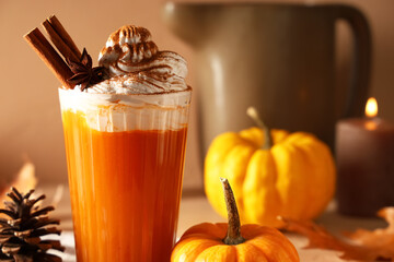 Glass of orange pumpkin latte with whipped cream and cinnamon on beige background, closeup