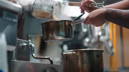 Tattooed chef preparing a pasta dish with a strainer and boiling water in a professional kitchen