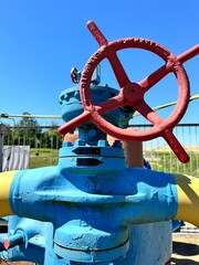 The photo shows yellow and blue gas pipes with a large red valve at the base, located outside in a field. The pipes supply gas to production facilities.