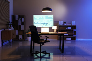 Interior of data scientist's office with workplace, shelving units, laptop and diagrams projection on wall