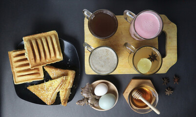 an assortment of hot drinks and snacks from indonesian cafe. pancong, toast, tea, milk, ginger, honey, egg, etc on black background