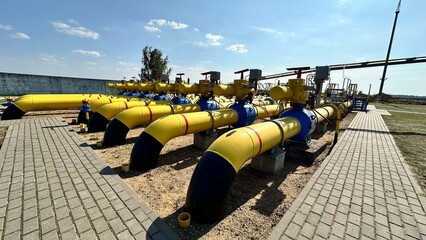The photo shows yellow and blue gas pipes with black stripes that enter the ground from above. Gas is supplied through the pipes under high pressure.