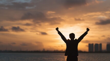 Fototapeta premium Silhouette of successful businessman with arms raised in triumph at sunset.