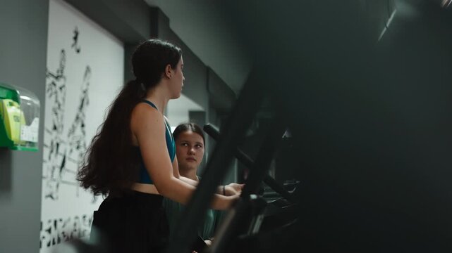 Personal trainer guiding a girl on elliptical machine in the gym