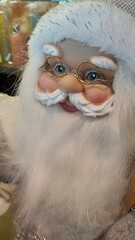 Close-up of a decorative Santa Claus figurine with a fluffy white beard, blue eyes, and golden...