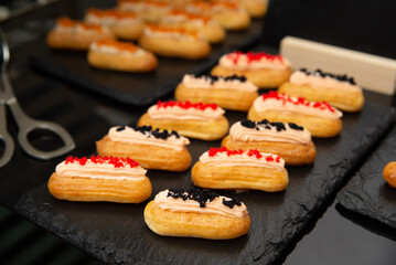 Gourmet eclairs on slate tray. A selection of gourmet eclairs arranged on a slate tray, topped with colorful icing and garnishes. 