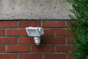 Outdoor motion sensor light attached to a brick wall near greenery