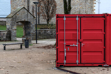 Red storage container in a serene outdoor area by historic buildings