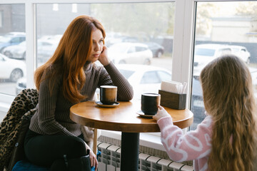 Pretty caucasian mother and her daughter sitting in the cafe and drinking cacao or coffee. Reading and looking at the book. Slow motion of cute young woman with her kid.
