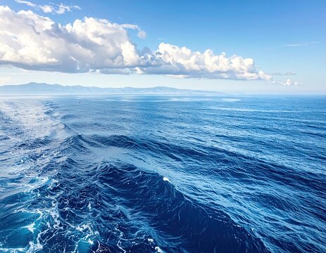 Vast Deep Blue Ocean Water Surface with White Waves and Clouds Against Clear Blue Sky in Sunny Weather