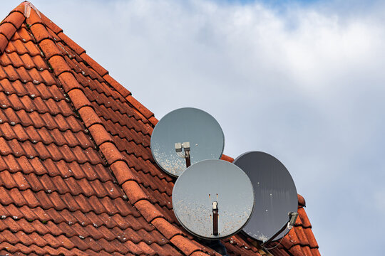 Satellite dishes installed on a red tiled roof against cloudy sky