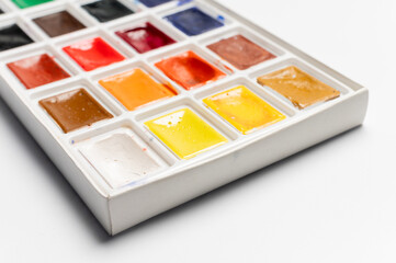 Watercolor packaging on a white background, side view from above. New paints have been opened for new work and painting. No one is in the photo, a close-up of the professional paints