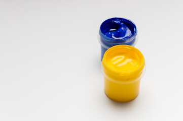 Small bottles of yellow and blue acrylic or gouache paints on a white background with space for text. Multicolored art supplies